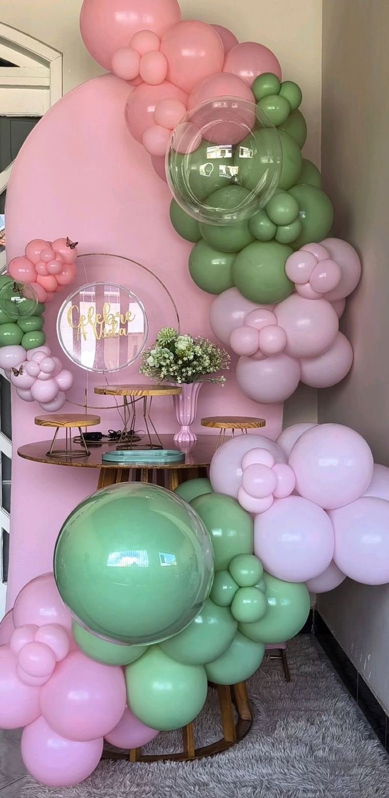 Decoração de festa com arco de balões em tons de rosa e verde e mesa de doces.