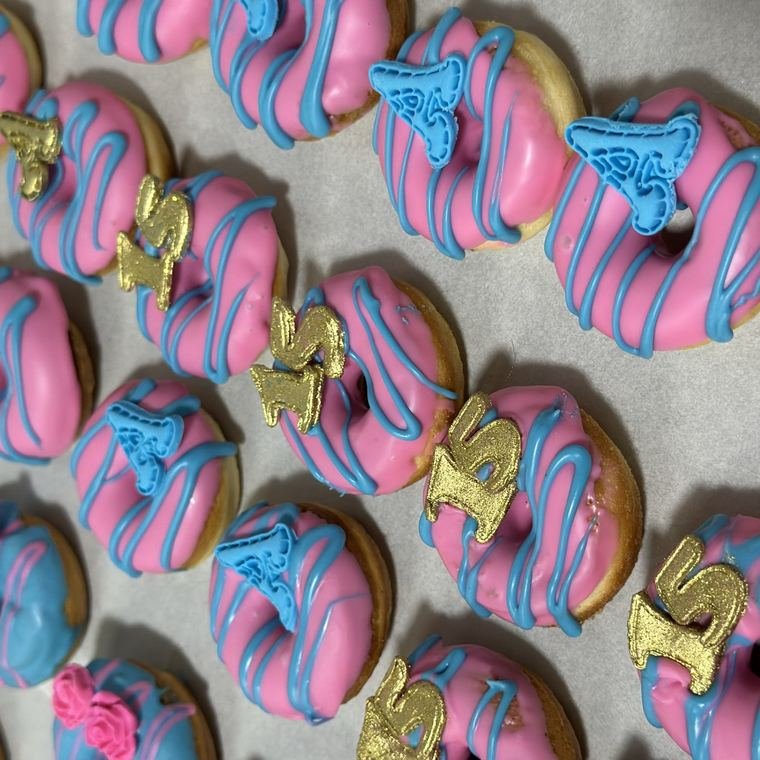 Mini donuts decorados em rosa e azul com detalhes dourados.